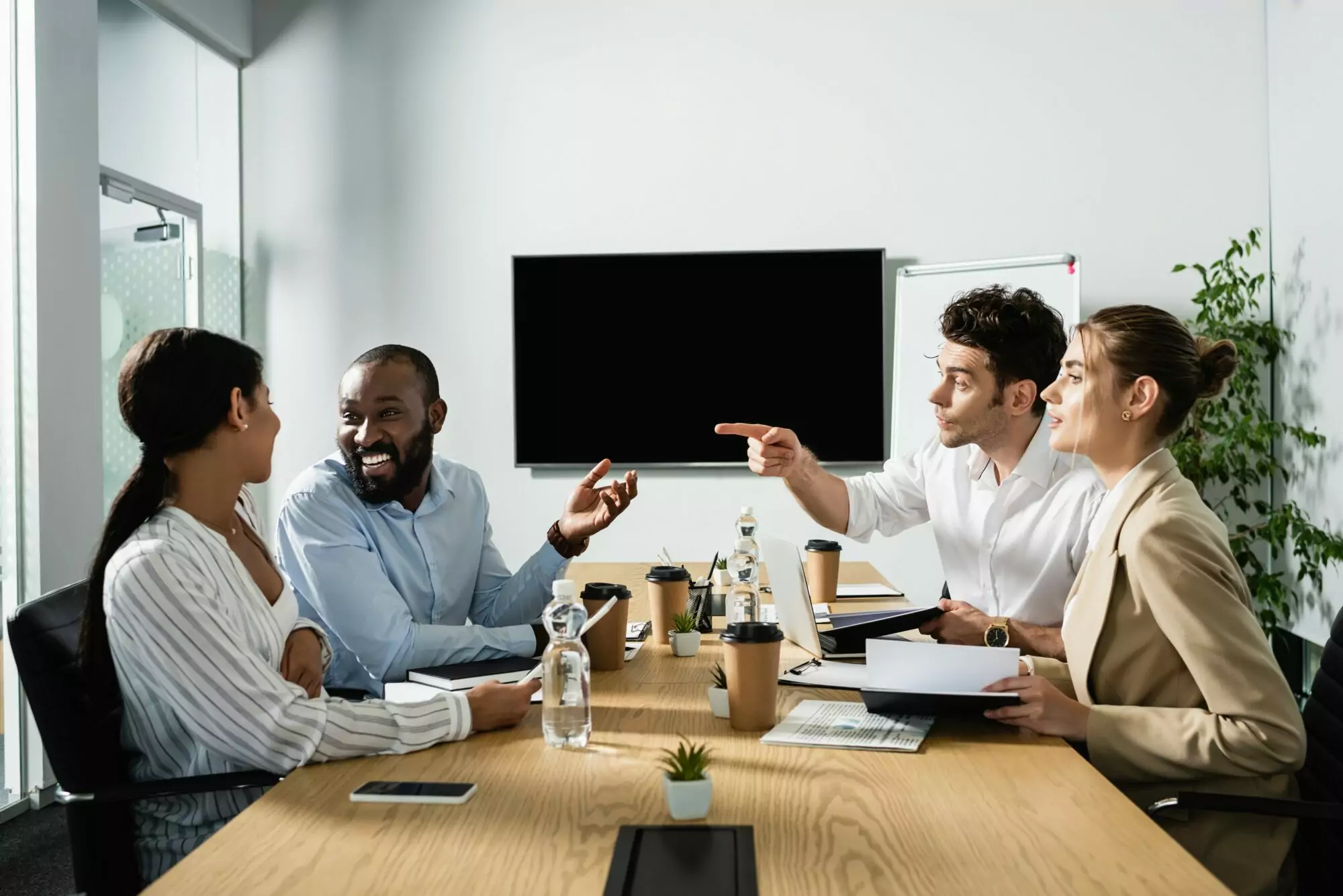 young businessman pointing with finger near cheerful multicultural colleagues